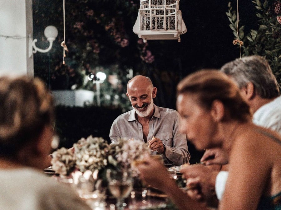 Tablée du soir en extérieur : des convives rient et discutent autour d’un bouquet, dans une lumière chaude.