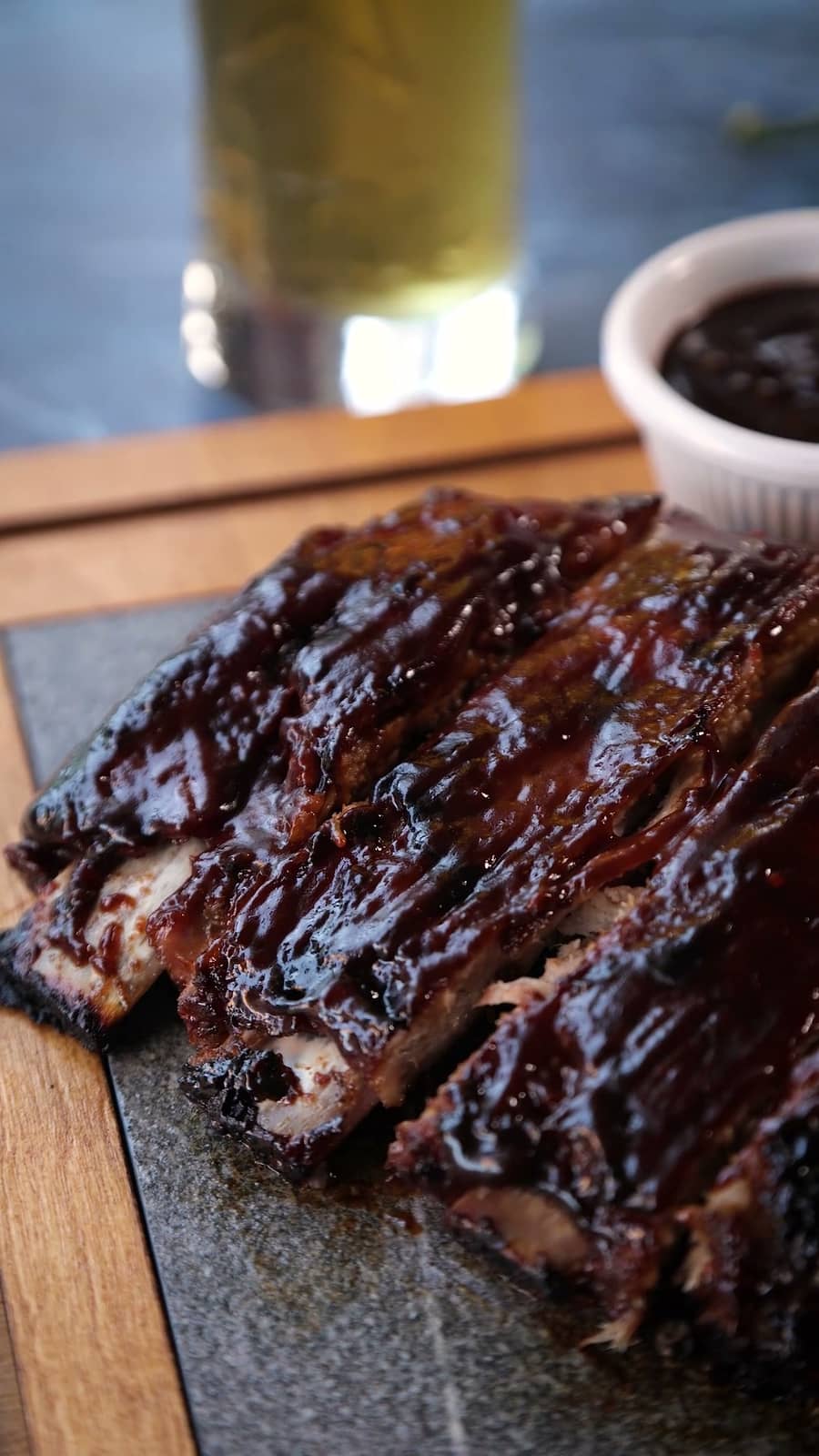 Travers de porc laqués et tranchés, dressés sur une ardoise avec un ramequin de sauce barbecue.