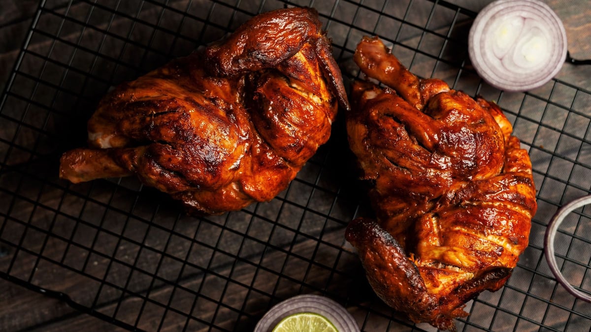 Deux demi-volailles laquées, la peau brillante et ambrée, posées sur une grille noire avec un demi-citron vert.