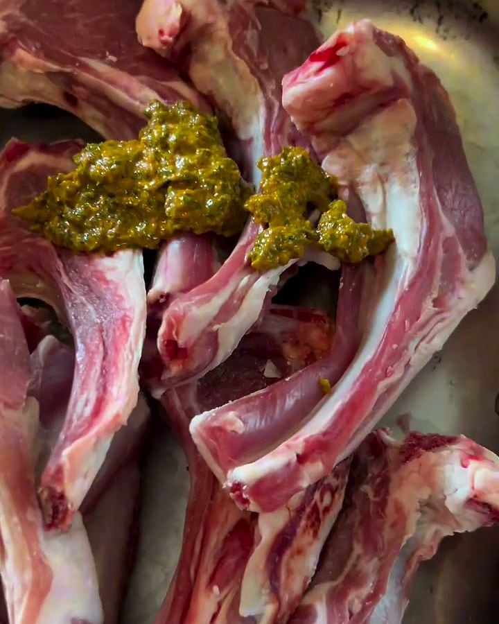 Côtes d’agneau crues, recouvertes d’une marinade verte aux herbes.