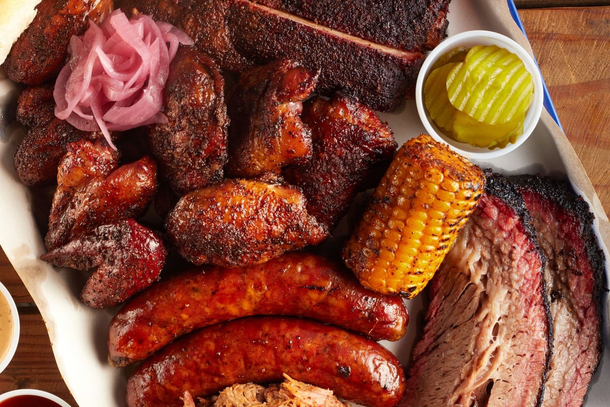 Plateau de partage vu de dessus : travers, saucisses, poitrine tranchée, épi de maïs et pickles.