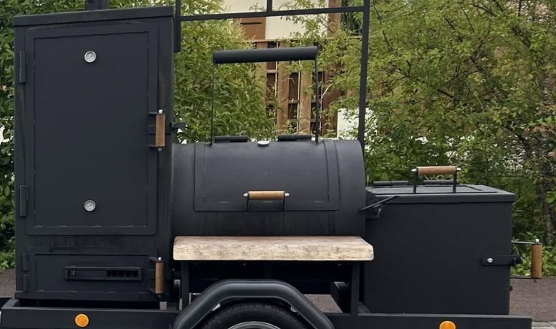 Le smoker Hunter X Smoker de profil : chambre de cuisson verticale à gauche, cuve horizontale au centre, foyer à droite et plan de travail en bois.