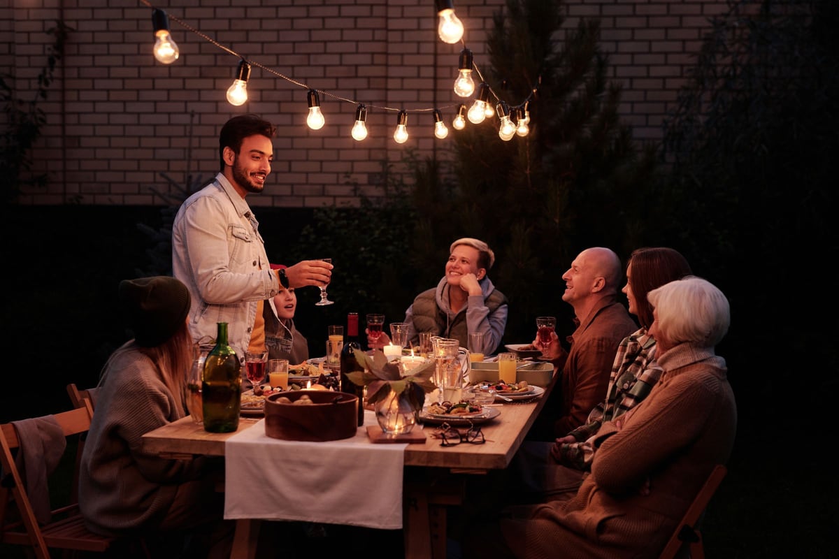 Tablée du soir dans un jardin, sous des guirlandes lumineuses : les convives rient et trinquent.