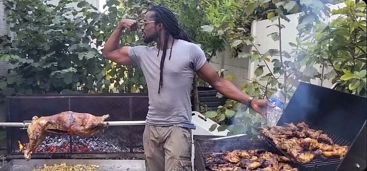 Cuisson en extérieur : une bête entière tourne à la broche au-dessus des braises, à côté d’un gril garni de viandes.