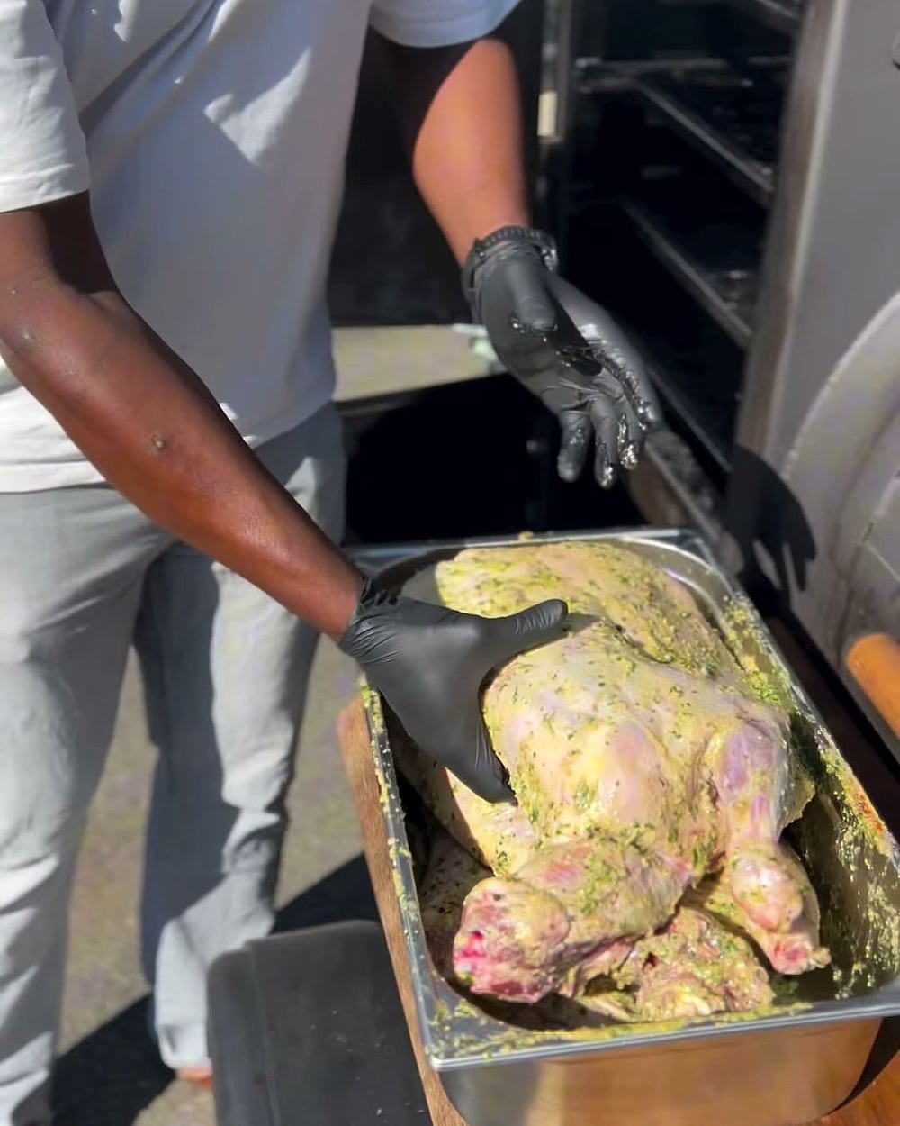 Yoann dépose une volaille entière marinée aux herbes dans un bac, devant le smoker ouvert.